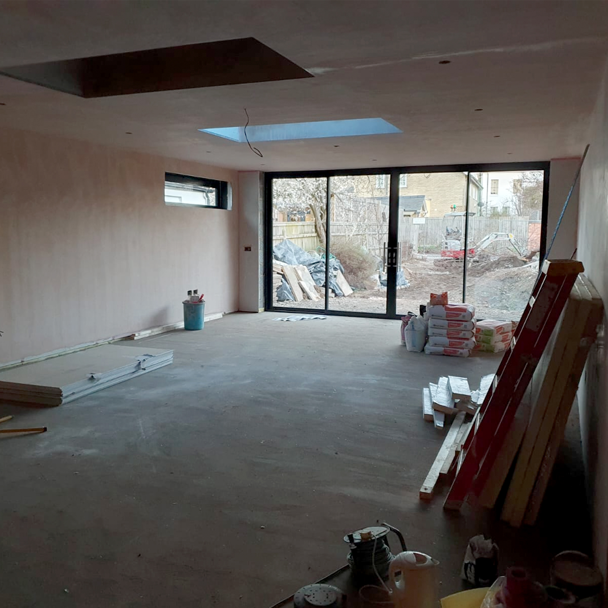 A photo of the interior of the extension with the large sliding glass doors in place, but the kitchen still under construction. The image shows the open-plan living area with the natural light flooding in from the garden. Construction materials and tools are visible in the foreground, giving viewers a sense of the work that went into creating the finished space. This photo highlights the potential of the extension and gives viewers a glimpse of what the finished product will look like.